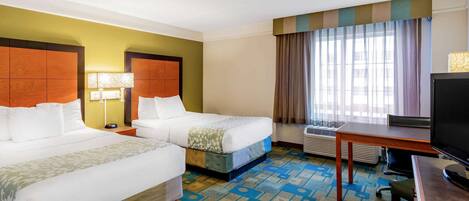A hotel room with two beds, a desk, a television, and a window with curtains.