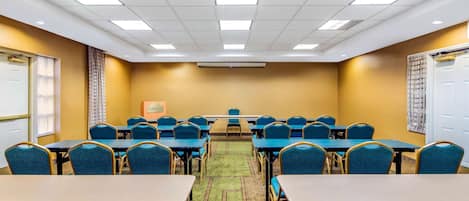 Un salón de conferencias con mesas y sillas, piso alfombrado y una pizarra en la pared.