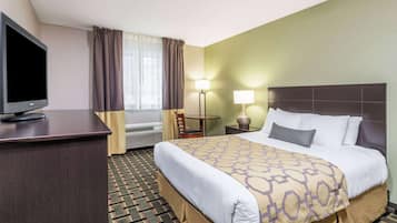 A hotel room with a bed, a desk with a TV, a chair, two lamps, and a window with curtains.