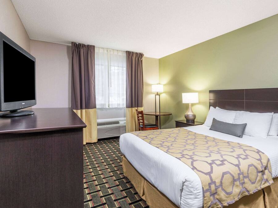 Ein Hotelzimmer mit Bett, Schreibtisch mit Fernseher, Stuhl, zwei Lampen und einem Fenster mit Vorhängen.