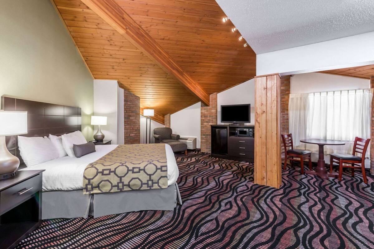 Habitación de hotel con cama, escritorio, silla, televisor y zona de comedor con mesa y sillas.
