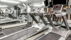 Un gimnasio con cintas de correr, máquinas de pesas y una pantalla digital.