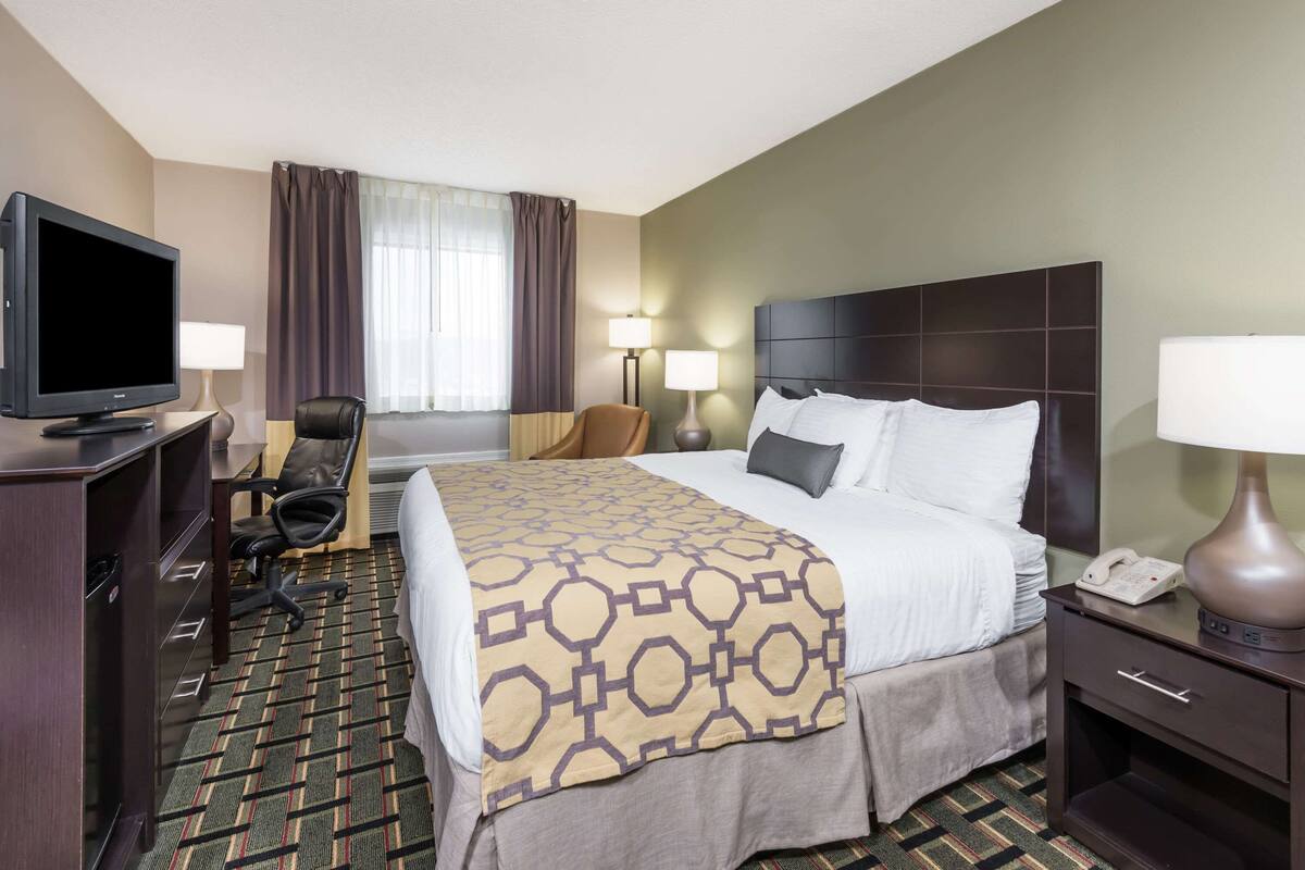 Una habitación de hotel con cama, escritorio con televisor, silla, lámpara y teléfono.