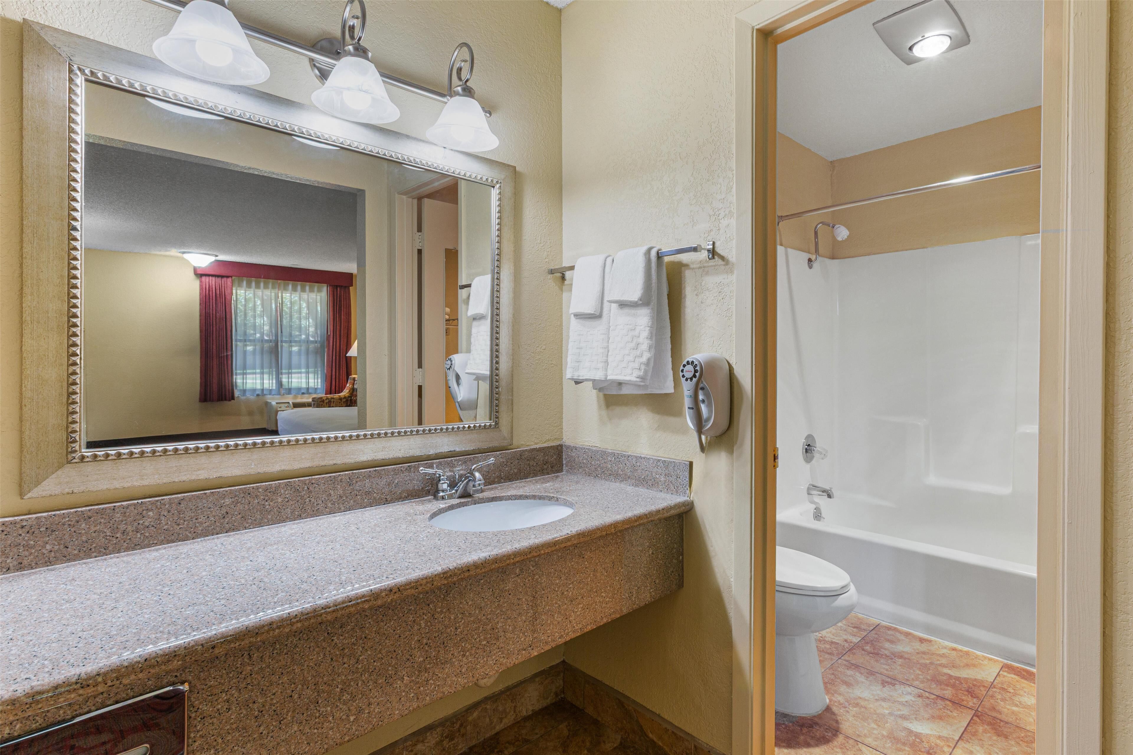 A bathroom with a granite countertop sink, a large mirror, a towel rack, and a white bathtub.