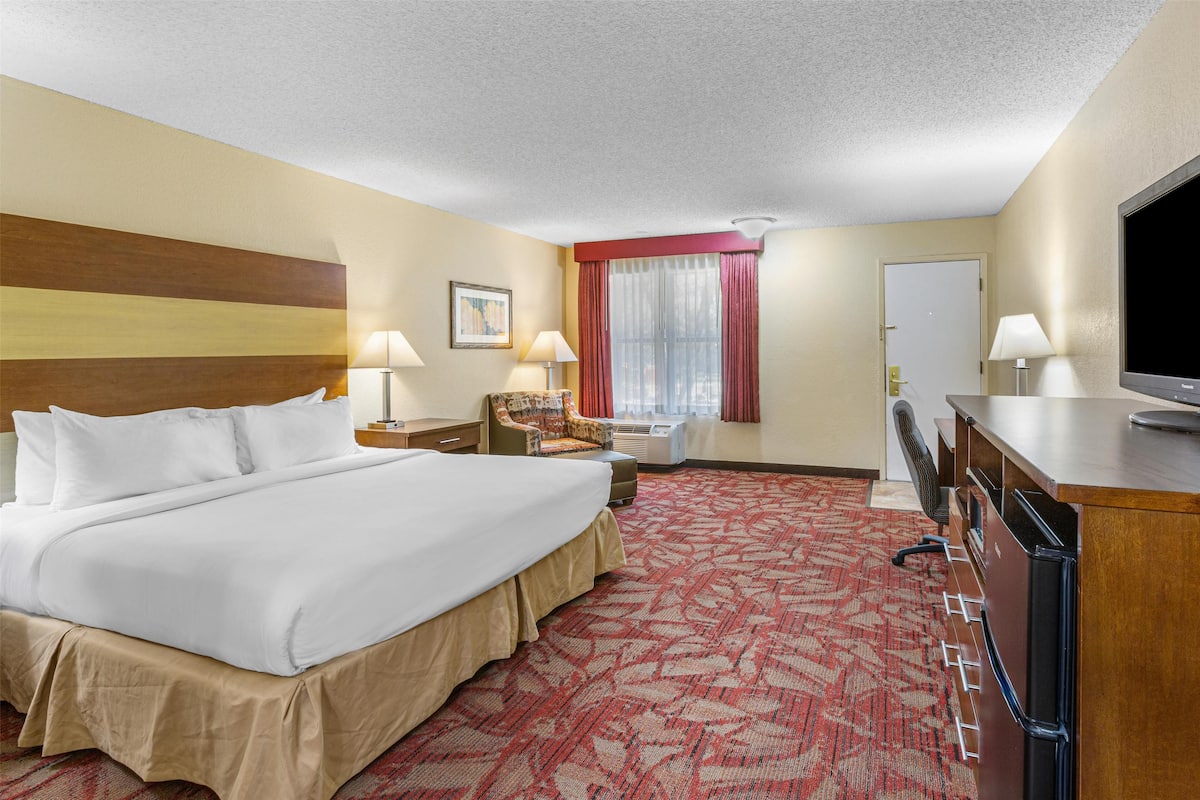 A hotel room with a large bed, a desk, a chair, a television, and a window with curtains.