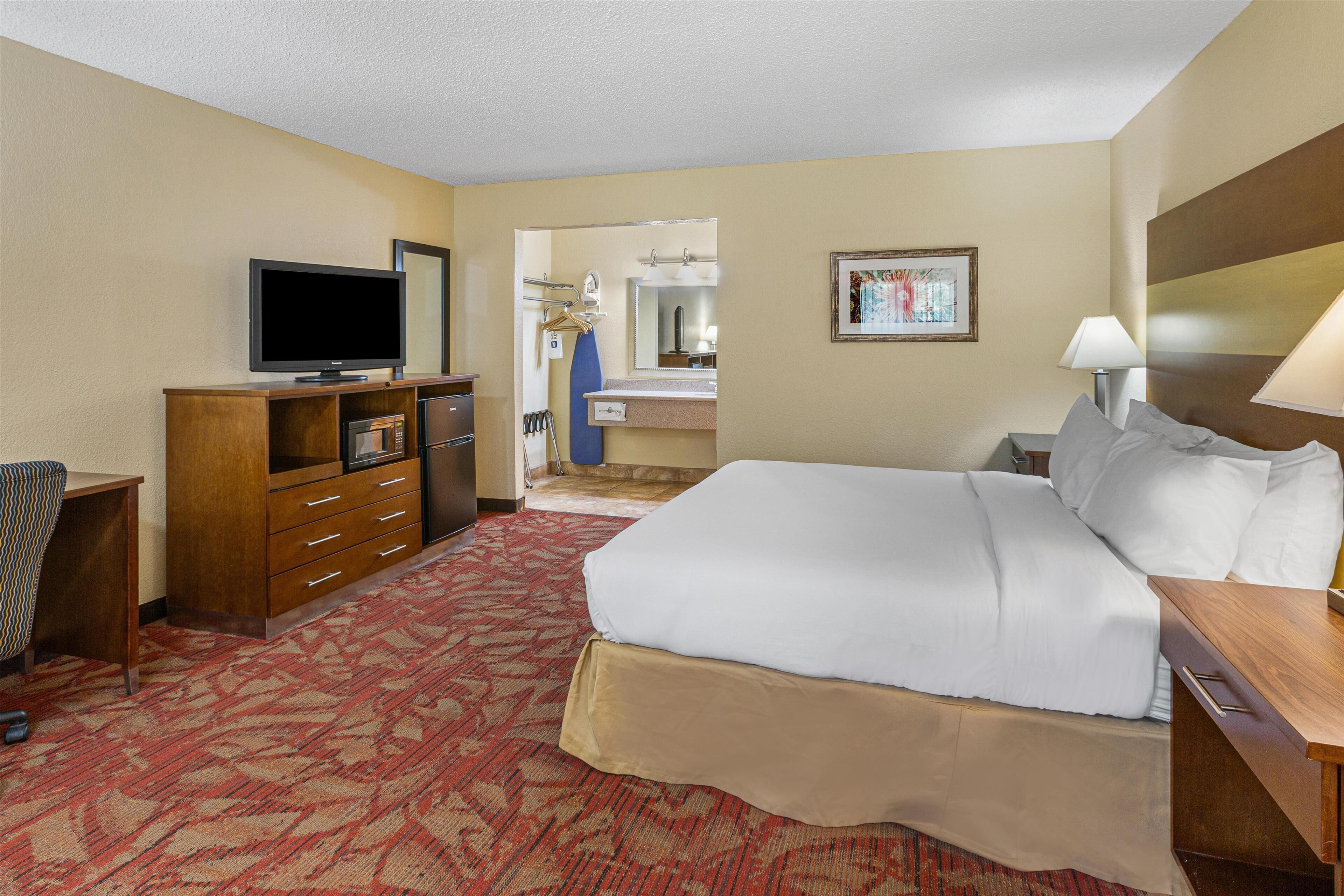 Habitación de hotel con cama, televisor, cómoda, espejo y piso alfombrado.