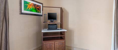 Una habitación de esquina con un escritorio de madera, una computadora y un cuadro en la pared.