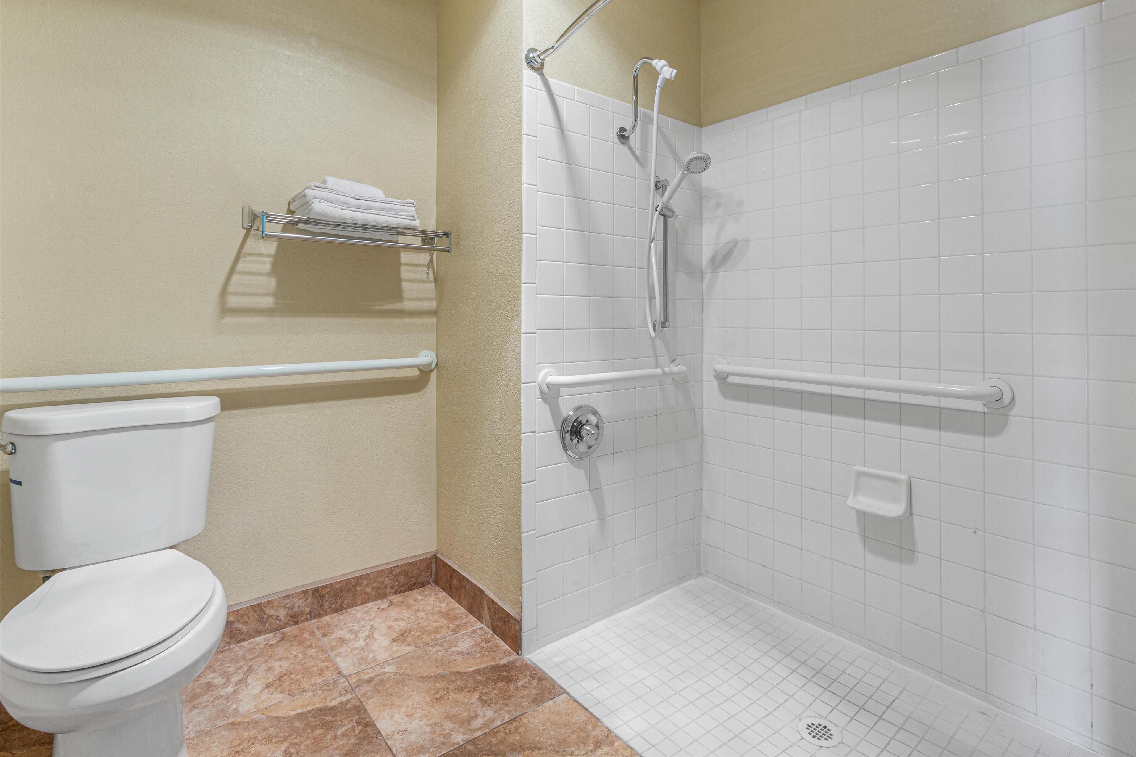 A bathroom with a toilet, a shower with grab bars, and a towel rack.