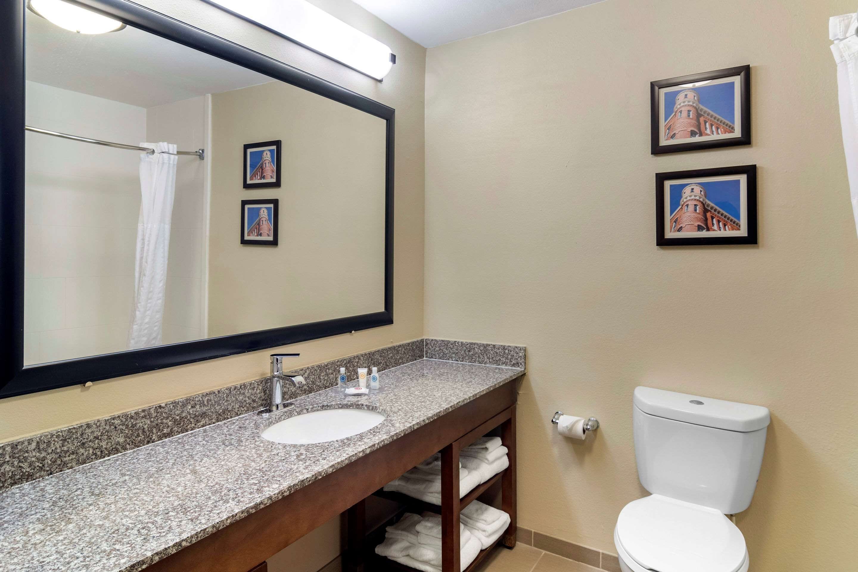 A bathroom with a granite countertop sink, a large mirror, a toilet, and two framed pictures on the wall.