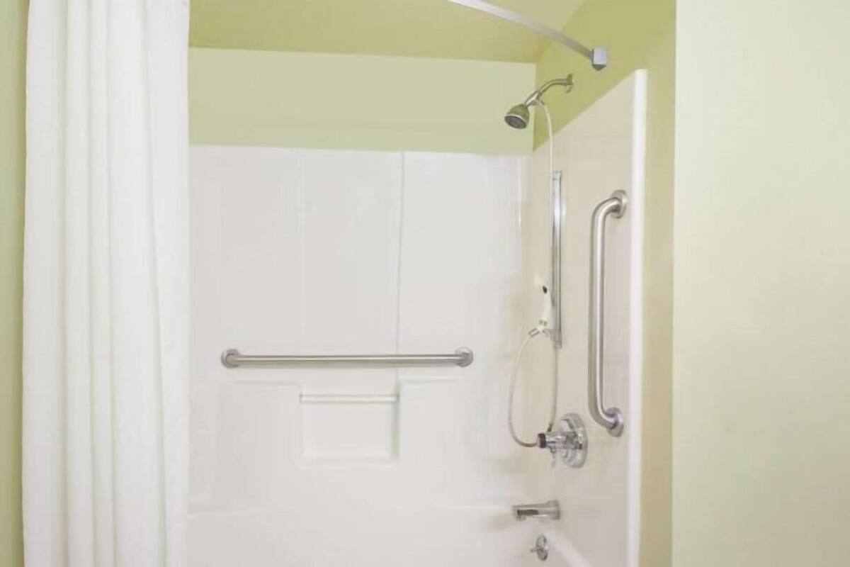 A bathroom with a white door, a shower with a handheld showerhead, and grab bars on the wall.