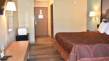 Quarto de hotel com uma escrivaninha de madeira, uma cama com colcha estampada e duas luminárias fixadas na parede.
