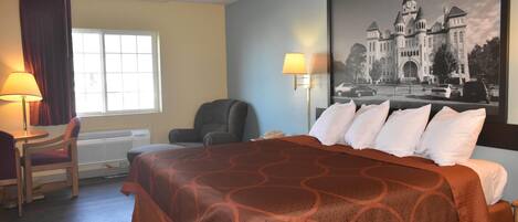Een hotelkamer met een groot bed, een bureau met een stoel, een raam met gordijnen en een wandlamp.