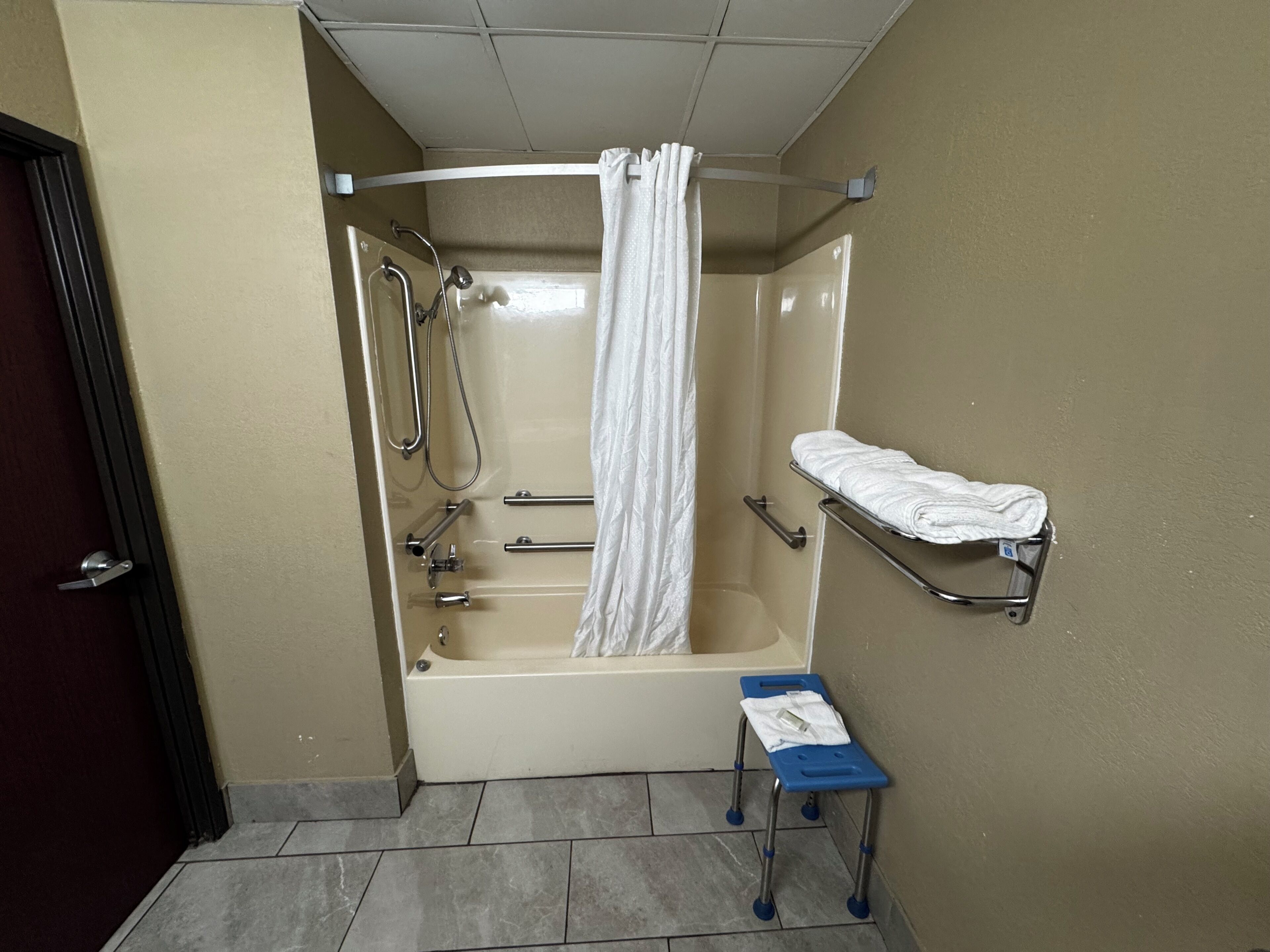 Un baño con bañera, ducha, toallero y un pequeño taburete.