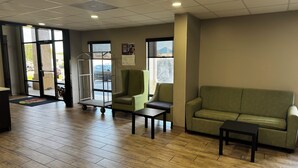 A lobby with a wooden floor, a green sofa, a small table, and a metal cart. - Super 8 by Wyndham Conway (Conway)
