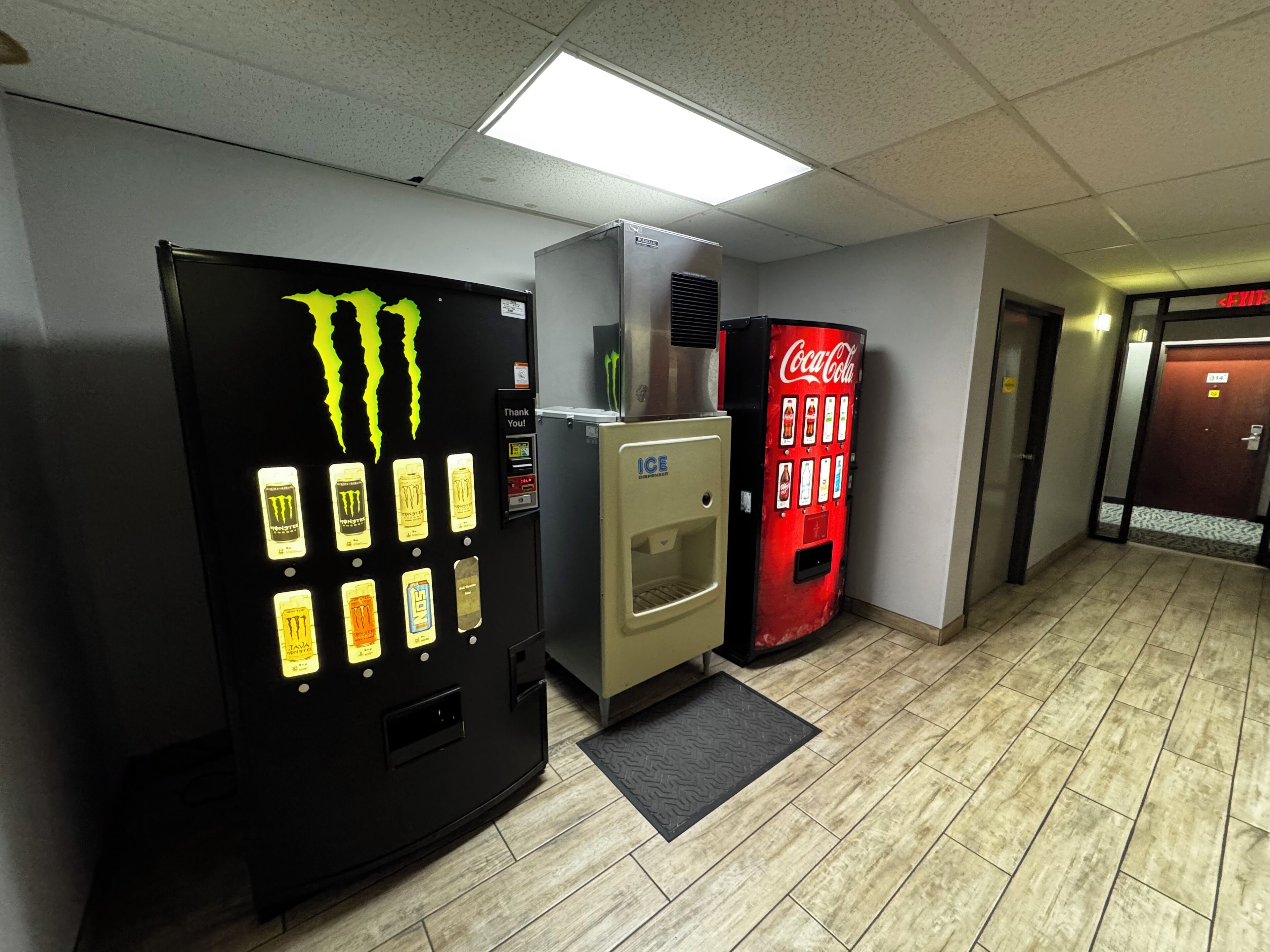 A hallway with a Monster energy drink vending machine, an ice dispenser, and a Coca-Cola vending machine.