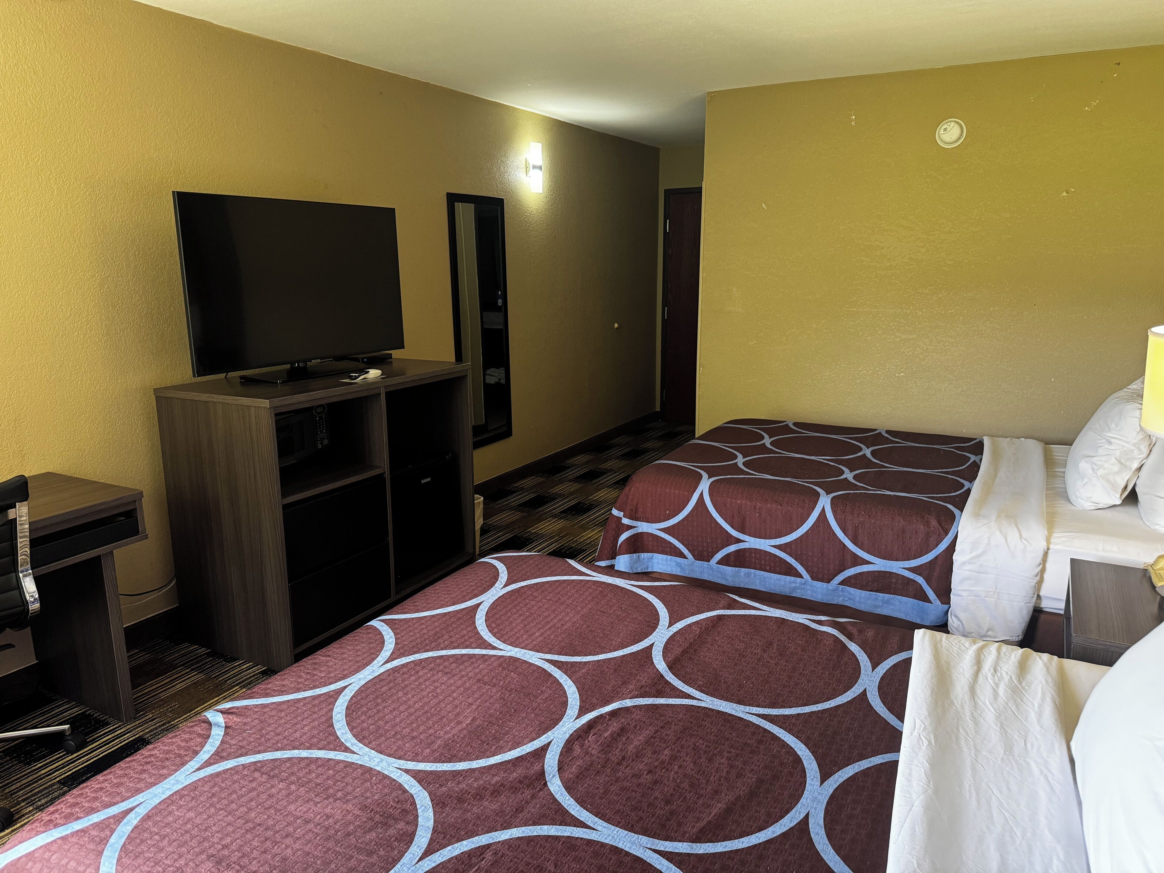 A hotel room with a bed, a TV, a desk, and a lamp.