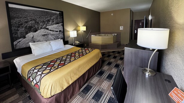 A hotel room with a bed, a large framed picture, a bathtub, and a desk with a lamp. - Super 8 by Wyndham Conway (Conway)