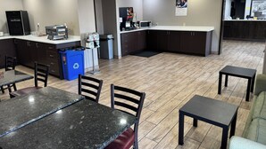 A modern kitchen area with a microwave, coffee machine, and a trash bin. There are wooden tables and chairs, and a small counter with a sink. - Super 8 by Wyndham Conway (Conway)