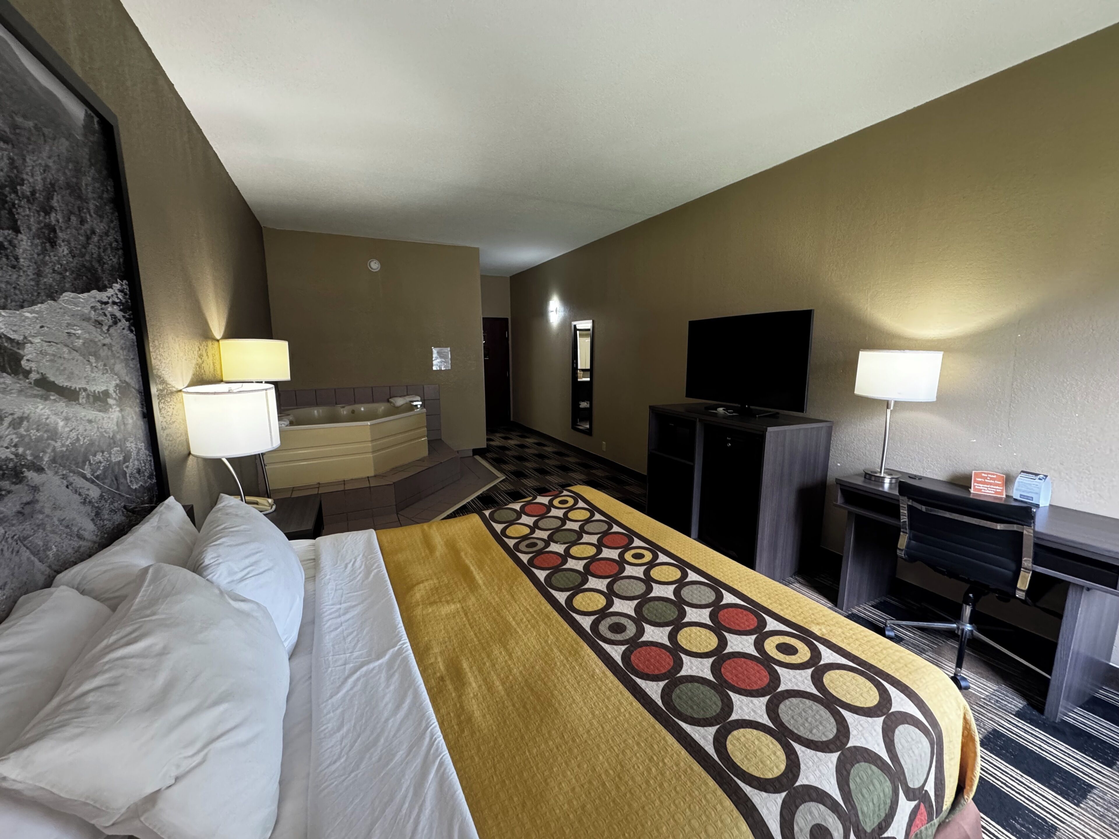 Habitación de hotel con cama, bañera, escritorio con televisor y lámpara de escritorio.