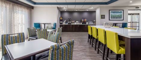 A modern hotel dining area with a long counter, multiple tables, and chairs.