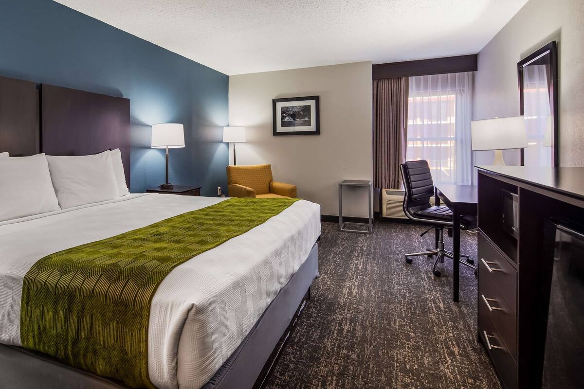 Une chambre d’hôtel avec un grand lit, deux chaises, un bureau et un tableau au mur.