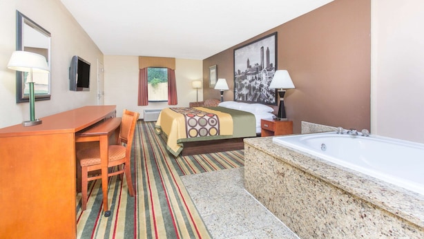 A hotel room with a bed, a desk, a chair, a large window, a bathroom with a bathtub, and a painting on the wall. - Super 8 by Wyndham Dublin (Dublin)