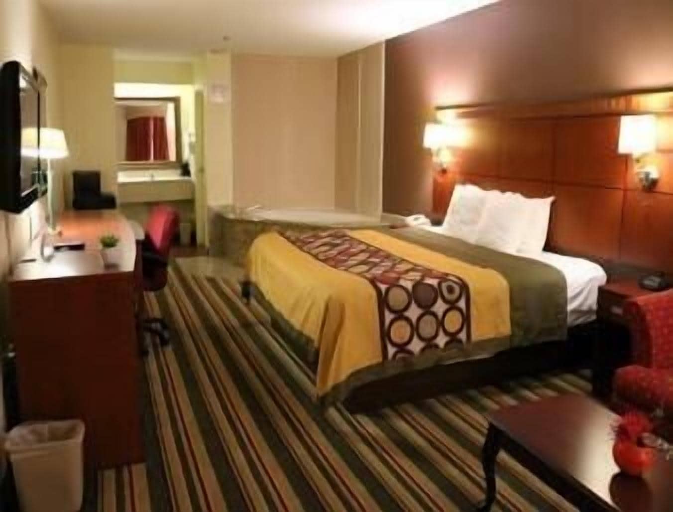 A hotel room with a bed, bedside table, lamp, and a small desk with a chair.