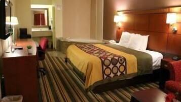 A hotel room with a bed, bedside table, lamp, and a small desk with a chair.