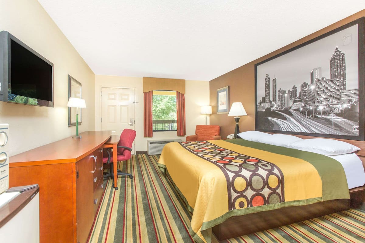 Ein Hotelzimmer mit Bett, Schreibtisch, Stuhl, Fernseher und einem großen Stadtbild an der Wand.