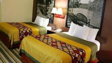 A hotel room with two beds, each with patterned bedspreads, a nightstand with a lamp, and a painting of a landscape on the wall.