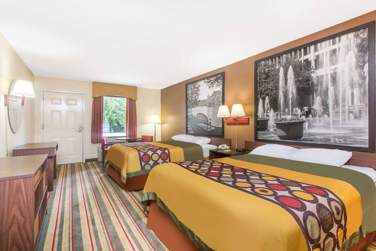 Ein Hotelzimmer mit zwei Betten, einem Schreibtisch, einem Stuhl, einem Fenster mit Vorhängen und zwei Wandleuchten.