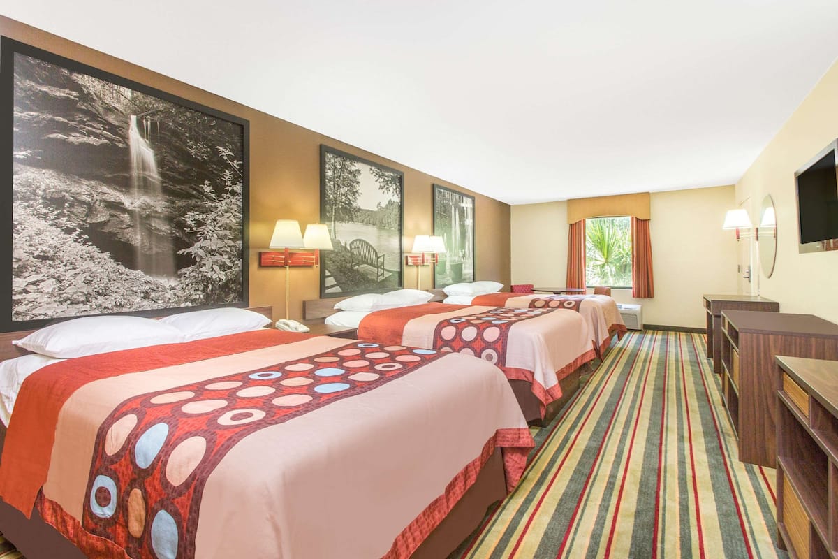 Ein Hotelzimmer mit drei Betten, einem großen Wandbild mit einem Wasserfall, einem Streifen Teppich und einem Fernseher an der Wand.