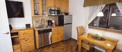 Cocina pequeña con armarios de madera, microondas, refrigerador, lavavajillas y una mesa de comedor con una silla.