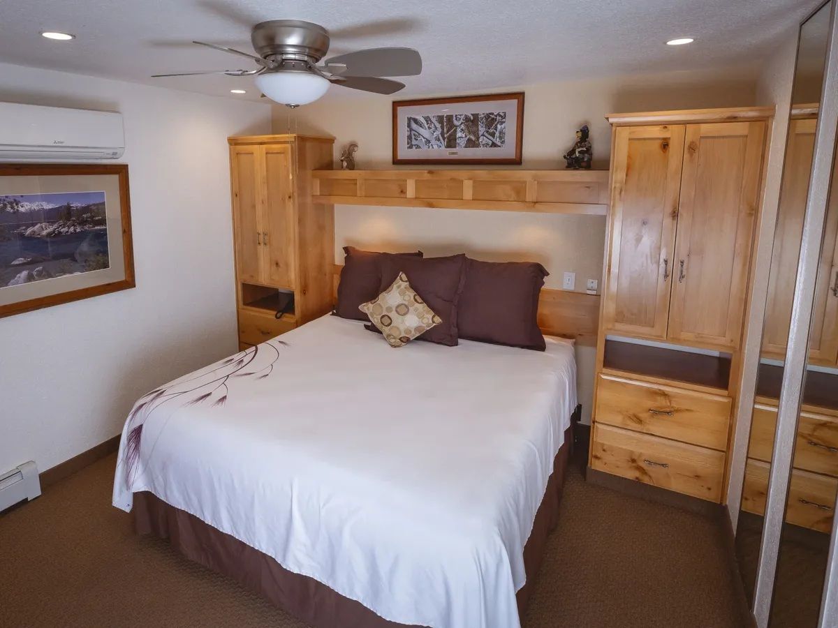 Ein Schlafzimmer mit einem Bett, Holzschränken, einem Deckenventilator und einem gerahmten Bild an der Wand.