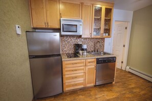 A kitchen with wooden cabinets, a stainless steel refrigerator, a microwave, a coffee maker, and a dishwasher. - Stardust Lodge (South Lake Tahoe)