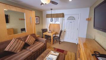 A living room with a sofa, a coffee table, a ceiling fan, a dining table with chairs, and a door with a window.