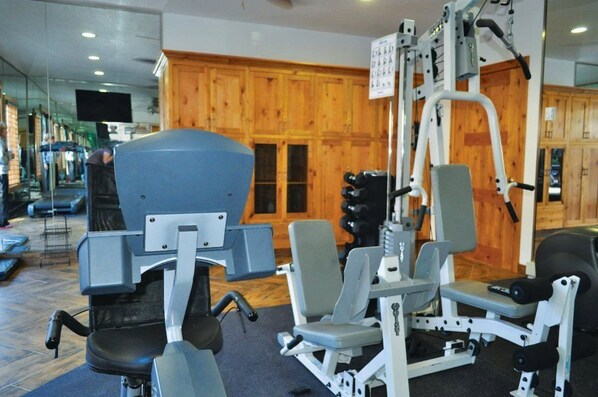 A gym with exercise equipment, wooden cabinets, and a large mirror.