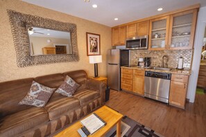 A compact living space with a sofa, a coffee table, a kitchen area including a refrigerator, microwave, and dishwasher, and a mirror with a decorative frame. - Stardust Lodge (South Lake Tahoe)