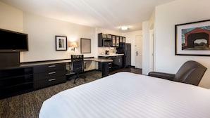 Une chambre d’hôtel avec un grand lit, un bureau avec une chaise, une kitchenette et un téléviseur.