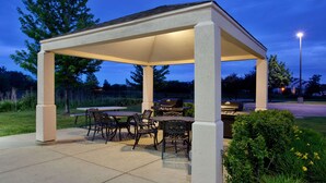 Une terrasse extérieure dotée d’un espace salon couvert, d’un barbecue et d’une table avec des chaises.