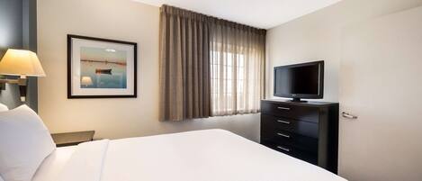 A hotel room with a large bed, a television on a dresser, a framed picture on the wall, and a window with curtains.
