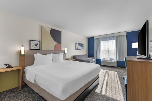 A hotel room with a large bed, bedside tables, a desk, a TV, and a window with curtains.