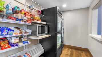 A compact kitchenette with a black refrigerator, microwave, and a small shelf with snacks.