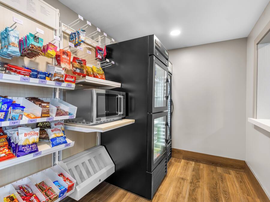 A compact kitchenette with a black refrigerator, microwave, and a small shelf with snacks.