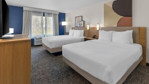 Une chambre d’hôtel avec deux lits, un bureau, une télévision et une grande fenêtre avec des rideaux.