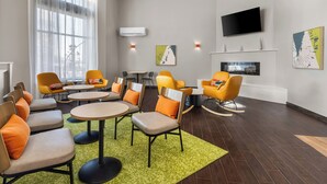 Une chambre d’hôtel moderne dotée d’un coin salon avec des fauteuils orange et des tables rondes, d’un téléviseur à écran plat fixé au mur et d’œuvres d’art accrochées aux murs.