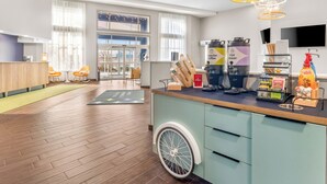 Un espace d’accueil moderne comprenant un comptoir d’accueil en bois, une rampe d’accès pour les personnes à mobilité réduite et un coin café avec une variété de boissons et d’accompagnements.