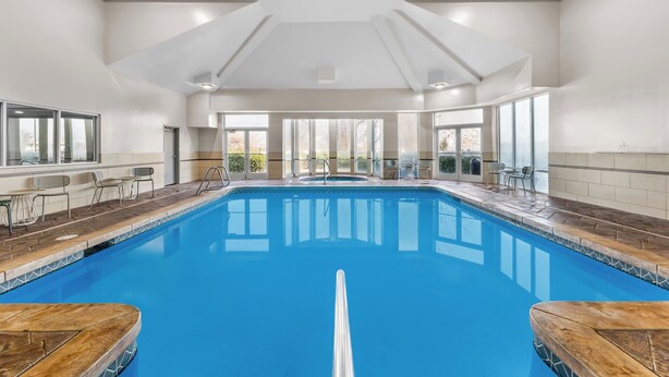 Une grande piscine intérieure à l’eau d’un bleu limpide, entourée de murs recouverts de carreaux et surmontée d’un haut plafond doté d’un éclairage encastré.