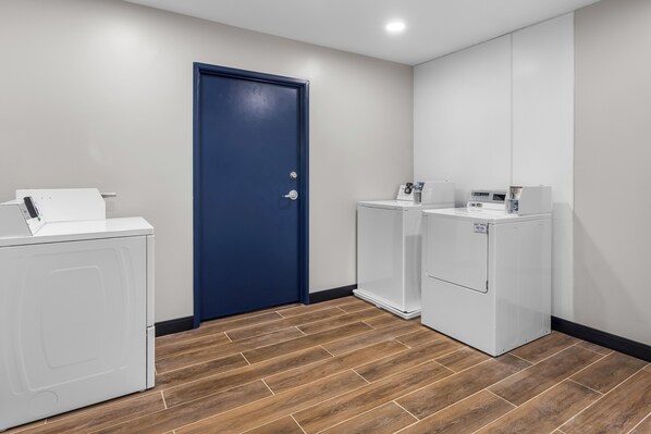 A laundry room with two white washers and dryers, a blue door, and wooden flooring.