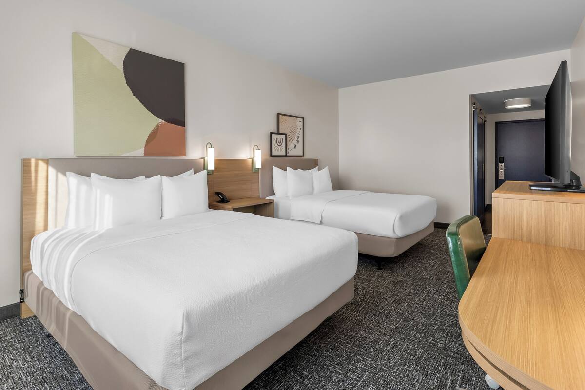 A hotel room with two beds, a desk, a television, and artwork on the wall.